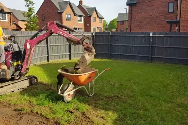 Small digger equipment in operation digging out turf on clay ground in residential garden.
