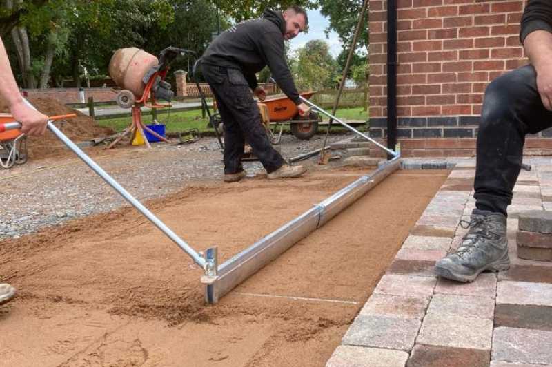 Landscaping works in Budbrooke, Warwick. Landscaping team on driveway works in progress. Driveway foundation work levelling sharp sand in preparation for laying tumbled block paving.