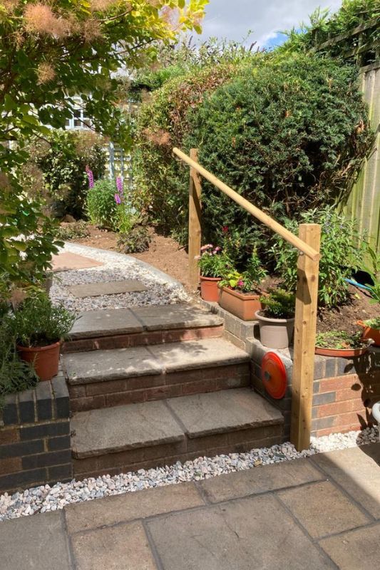 Landscaping works completed in Solihull. Natural stone patio with steps and timber hand rail leading up to natural stone pathway in upper level of garden transformation works.