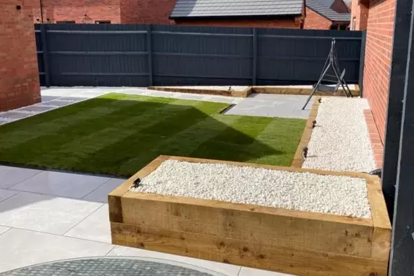 Raised planting beds built of timber sleepers and raised porcelain patio in new build garden with Porcelain paving pathways, decorative stone and block edge border around grass lawn.