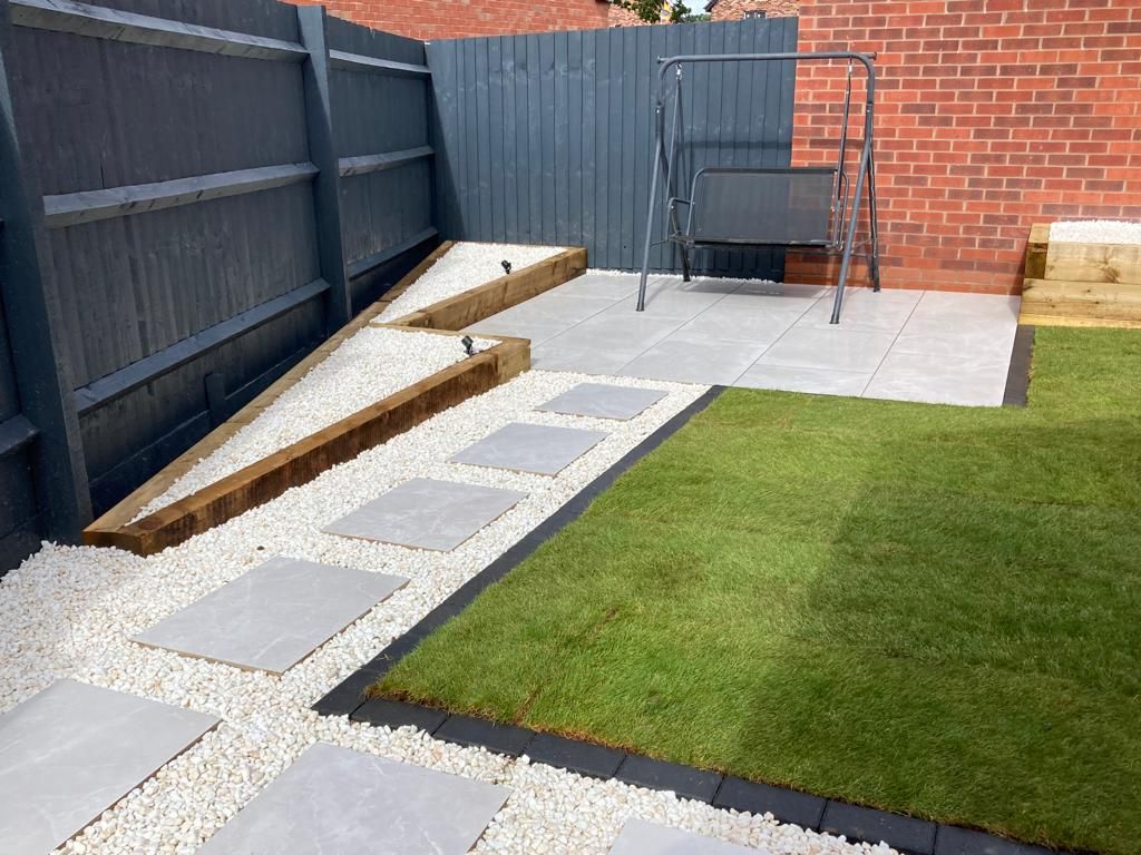 Contemporary new build home garden design and build with porcelain patio, porcelain pathway, raised sleeper beds, water feature and low voltage garden lighting for outdoor living space in Blythe Valley, Solihull - Oakland Group.