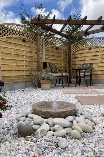 Decorative stone gravel, cobbles and water feature with new patio area with seating, decorative fencing and lighting.