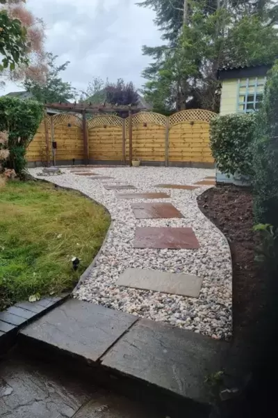 Decorative gravel path with sandstone paving slabs laid as stepping stones in path leading to new patio area with decorative fencing and lighting.