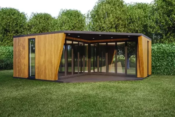 Modern contemporary design prefabricated large garden room installed in lush garden with mature hedges and trees.