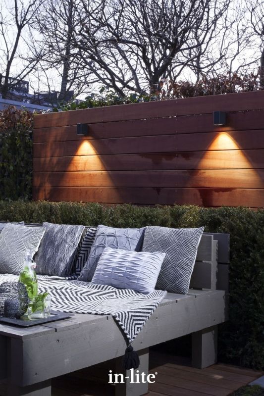 in-lite ACE DOWN DARK 12v outdoor wall lights, mounted on fence panel, illuminating decorative outdoor lounge seating area with a targeted beam of light downwards. Low voltage outdoor garden lights, atmospheric lighting for ambiance.