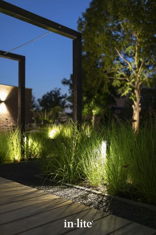 in-lite ACE HIGH DARK 12v outdoor bollard lights, positioned upright along a pathway border, illuminating through tall grasses along the border and pathway with a targeted light spread either side of the fixture. Low voltage outdoor garden lights, atmospheric path lighting for ambiance.
