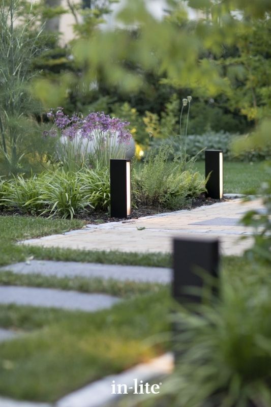 in-lite EVO LOW DARK 12v outdoor bollard lights, positioned upright in pathway border, illuminating along the pathway with a considerable amount of light without glare. Low voltage outdoor garden lights, atmospheric lighting for ambiance.