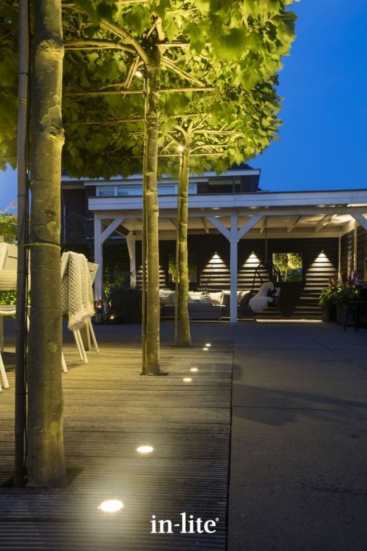in-lite FLUX 12v outdoor decking lights, recessed in decking boards along border of alfresco dining space, illuminating row of pleached trees with a strong and focused light from the ground up. Low voltage outdoor garden lights, atmospheric lighting for ambiance.