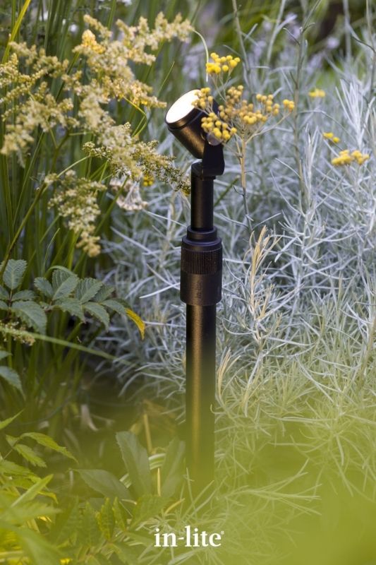 in-lite MINI SCOPE 12v outdoor spotlight and RISER-2 Spotlight Mounting Accessory with ground spike, positioned in soil, with elevated and tilted lighthead illuminating taller plants in planting bed. Low voltage outdoor garden lights, atmospheric lighting for ambiance.