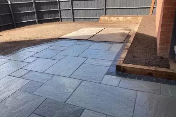 New patio laid with Kandla grey sandstone paving slabs, block edge border and raised planting beds built of timber sleepers.