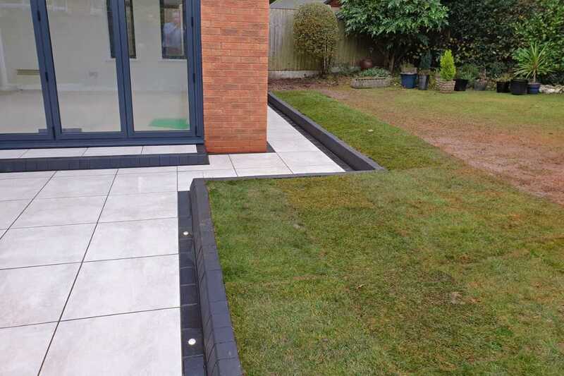 Contemporary style porcelain patio and block edge paving with integrated low voltage outdoor recessed lights.