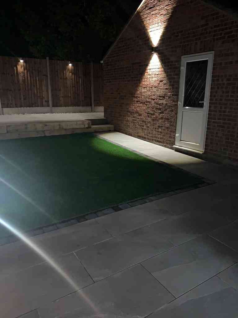 Low maintenance garden at night with outdoor porcelain raised patio terrace, new fencing and 12v lighting installed in Kenilworth, Warwickshire - Oakland Group.
