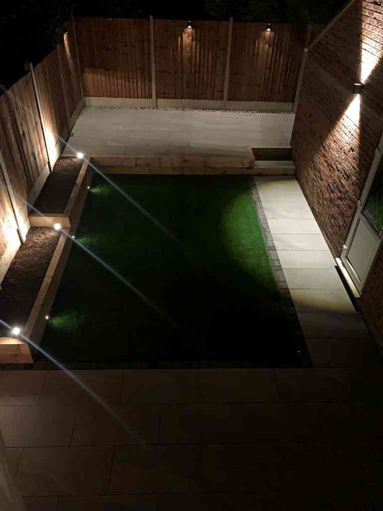 Low maintenance garden at night with outdoor porcelain, artificial lawn, raised patio terrace, new fencing and 12v garden lighting installed in Kenilworth, Warwickshire - Oakland Group.
