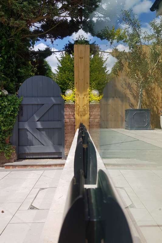 Landscaping works in Knowle, Solihull. Glass balustrade installation works completed. Close up of frameless glass balustrade system with toughened laminate glass panels and adjustable glass clamps installed and aligned onto raised patio for safety and aesthetics.