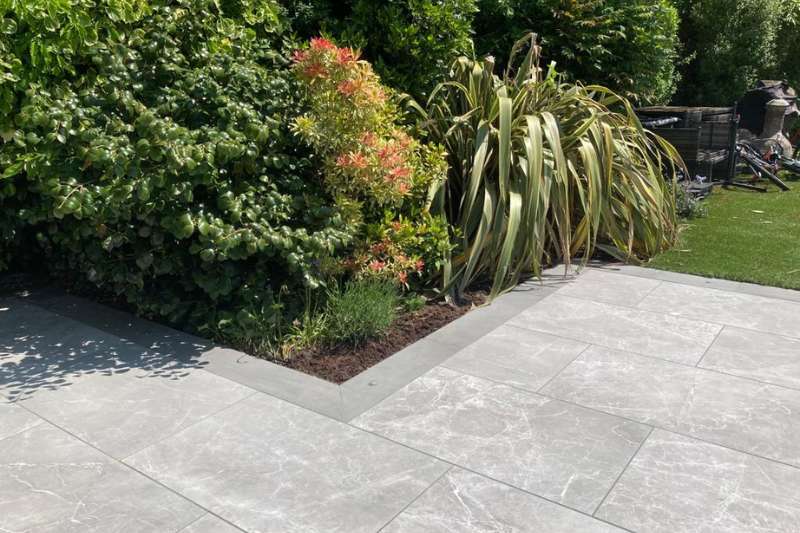 Landscaping works in Dorridge, Solihull. New porcelain patio build completed with low voltage outdoor lighting installed. Prima porcelain outdoor tiles. Main patio consists of 2cm Marble Light Grey 60 x 90cm. Patio border consists of 2cm Cemento Grey 45x90cm. in-lite PUCK 22 12v outdoor decking lights recessed in paving border around main patio.