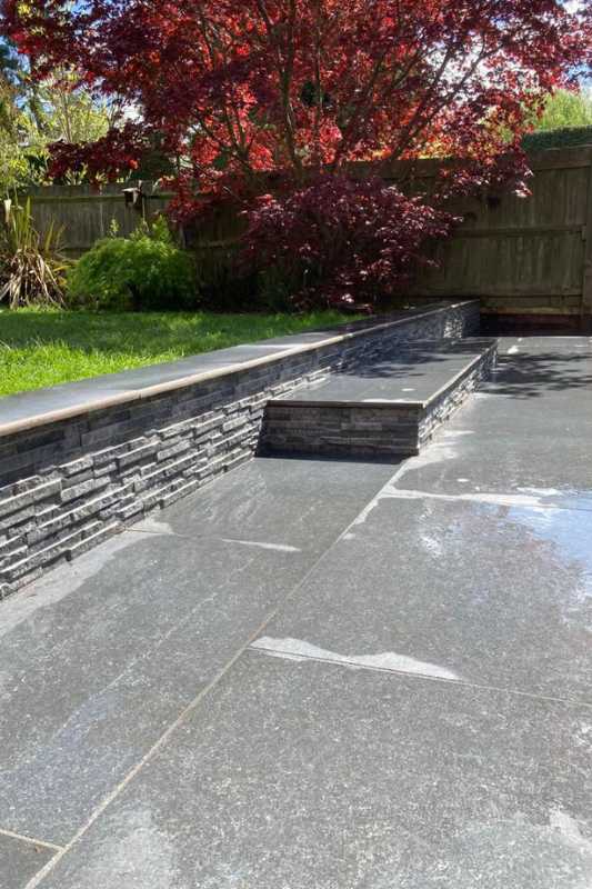 Patio landscaping works in Solihull. New patio and wall build complete with stone paving, steps, stone cladded wall and coping stone edging along the walling.