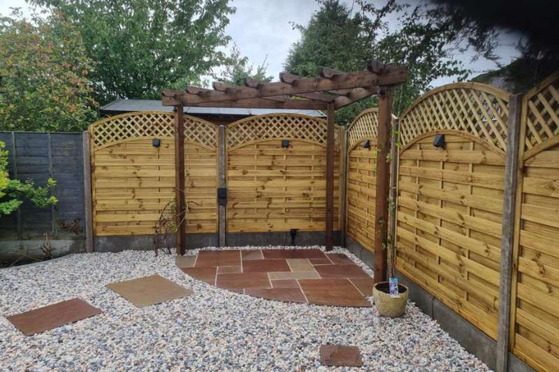 Natural stone pathway leading to natural stone patio area complete with pergola, curved trellis fencing panels and in-lite 12v outdoor wall lights mounted on fence panels.