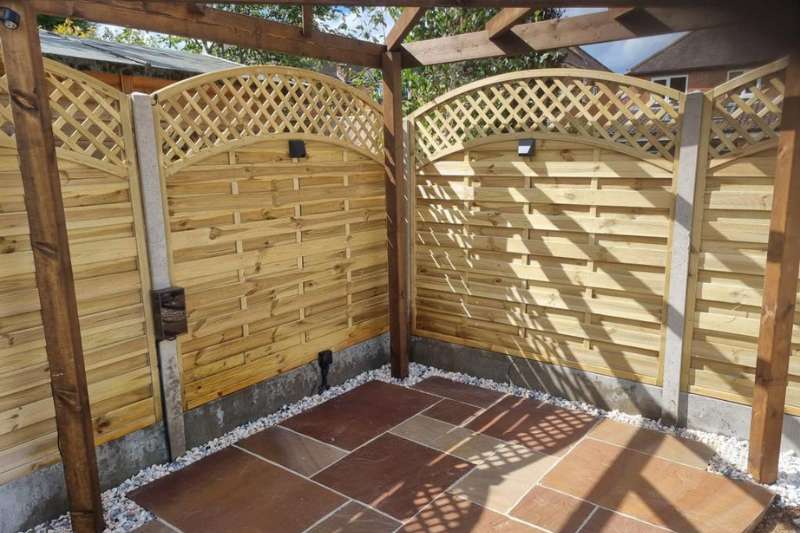 Natural stone patio area complete with pergola, curved trellis fencing panels and in-lite 12v outdoor wall lights mounted on fence panels.