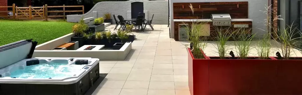 Large terrace porcelain patio outdoor living spaces complete with kitchen, jacuzzi, sunken decking area with iroko bench seating and fire table installed using the iGarden light steel subframe foundation system.