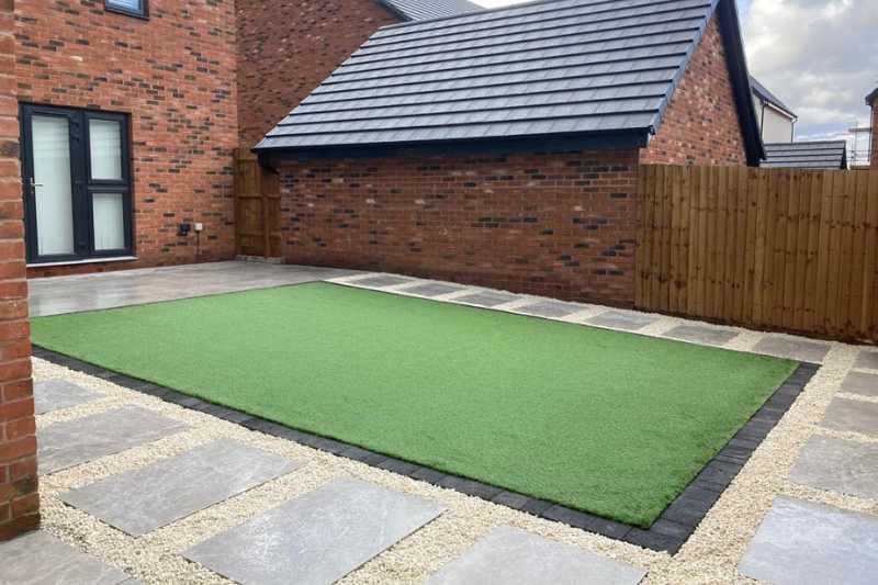 New build garden landscaping works, porcelain patio and pathways with block edge and decorative gravel surrounding artificial lawn in the new build garden. Bloor Homes at Blythe Valley, Solihull - Oakland Group.
