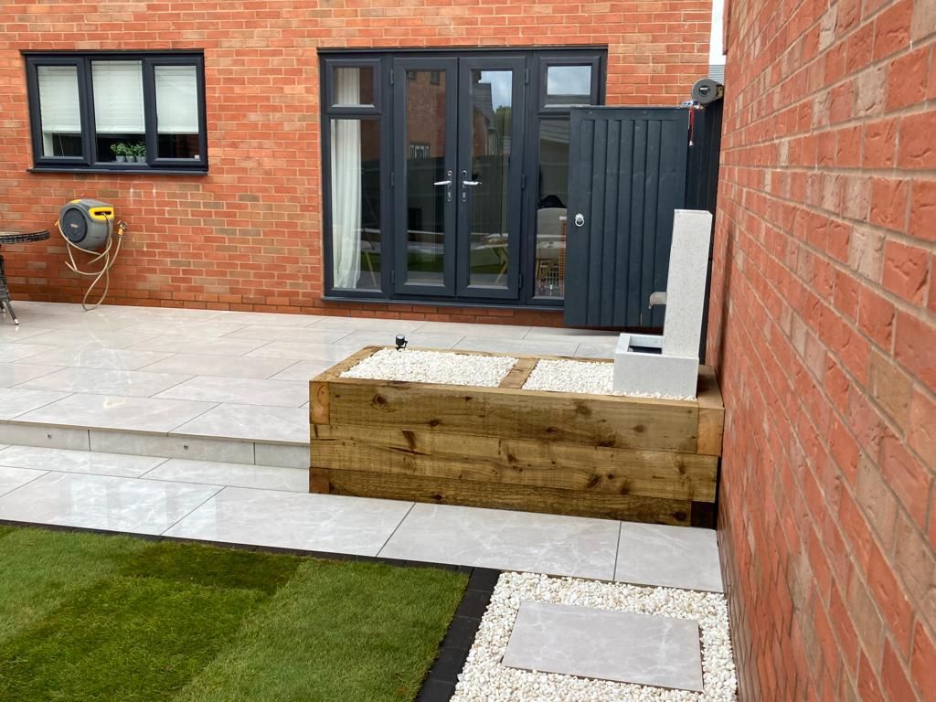 Contemporary new build home garden design and build with porcelain patio, porcelain pathway, raised sleeper beds, water feature and low voltage garden lighting for outdoor living space in Blythe Valley, Solihull - Oakland Group.