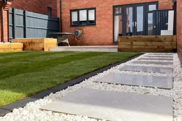Porcelain paving pathway with decorative stone, block edge border around grass lawn, raised planting beds built of timber sleepers and raised porcelain patio in new build garden.
