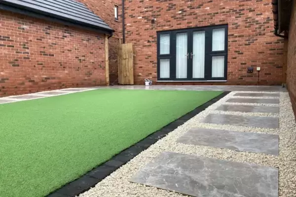 Porcelain paving pathway with decorative stone, block edge border around artificial lawn and porcelain patio in new build garden.
