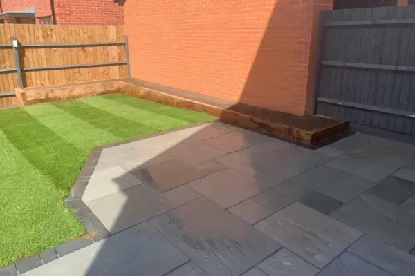 New patio Kandla grey sandstone paving slabs, block edge border, newly turfed lawn, fencing and raised planting beds installed.