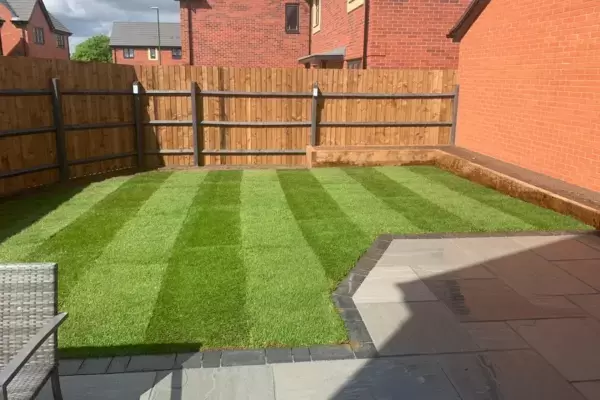 New patio laid with Kandla grey sandstone paving slabs, block edge border, new lawn, fencing and raised planting beds built of timber sleepers installed.