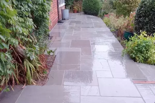 New patio and pathways built of natural stone paving slabs installed at the top of a sloping garden with planted borders.