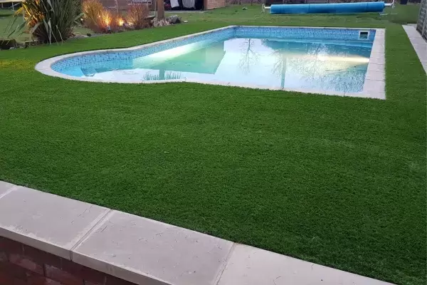 Swimming pool with artificial lawn and borders built with CED coping stones installed on retaining wall.