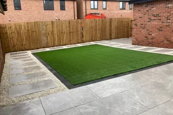 Porcelain patio and porcelain pathways with decorative borders around artificial grass area in low maintenance garden.