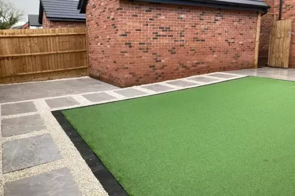 Porcelain patio and porcelain stepping stone paths interlinking around artificial grass area with block edge border in low maintenance garden.