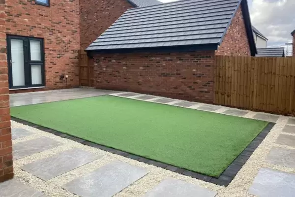 Porcelain patio and porcelain pathways interlinking around artificial grass area with block edge border in low maintenance garden.