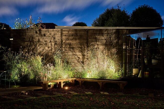 Bench seating and planting border illuminated from the ground up in garden.