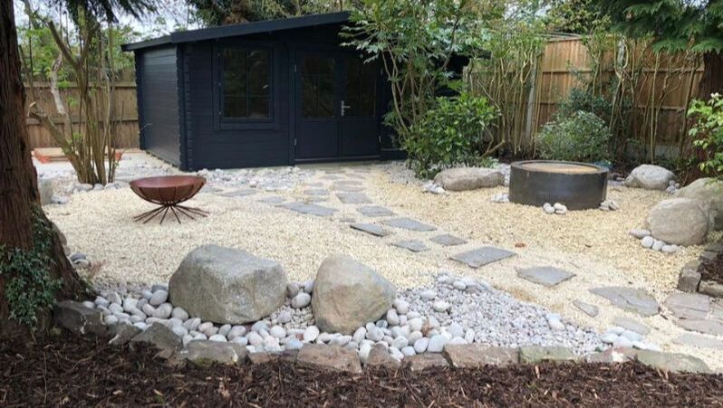 Landscaping works completed in Solihull. New gravel feature area with 'Cracked River bed' footpath leading to contemporary outbuilding gym. Scottish Beach Cobbles and Scotish Boulders. Large Corten steel fire bowl in situ.